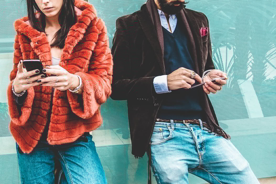 Woman in orange jacket and man looking the SEO trends 2024 on their phones.